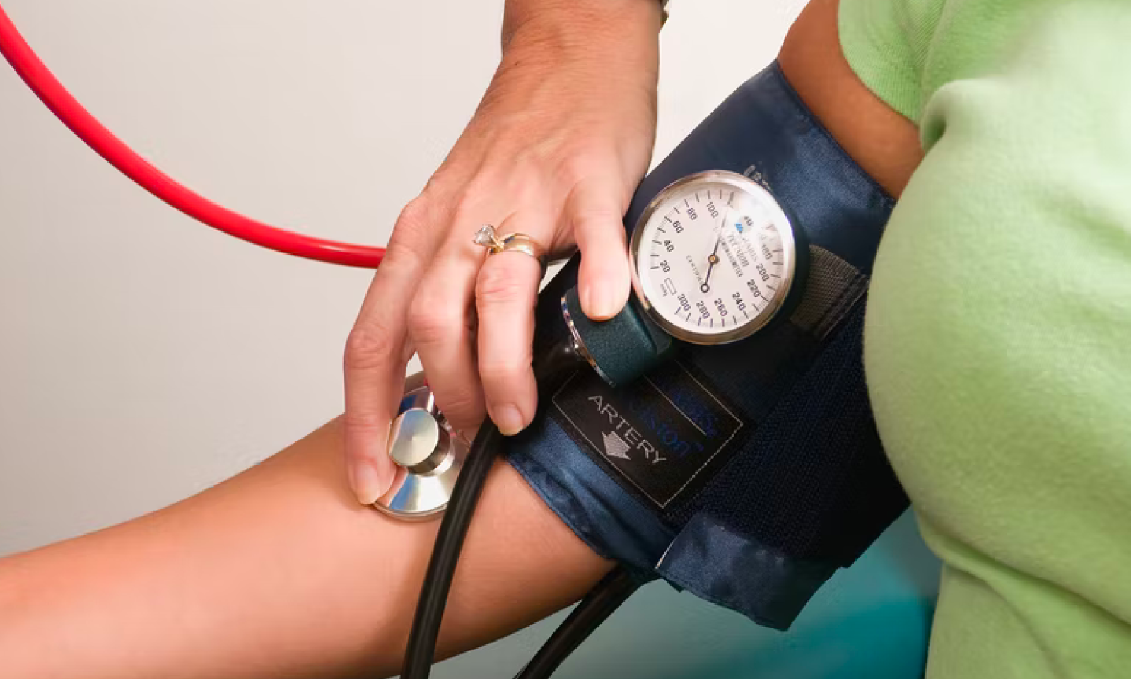 A woman has her blood pressure taken by another person, using a blood pressure monitor band.